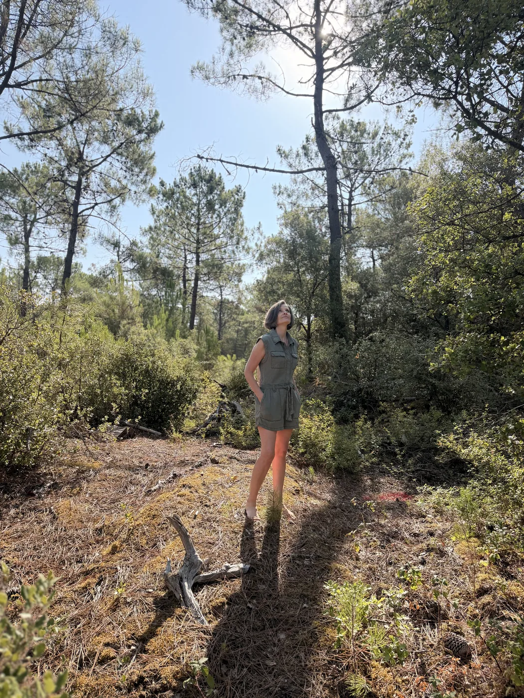 Sandra debout dans une clairière de pins, en pleine lumière